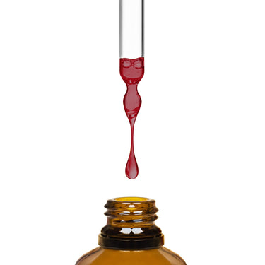 A dropper dripping clear red liquid into an amber bottle