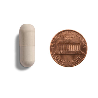 A off-white capsule being compared to the size of a penny