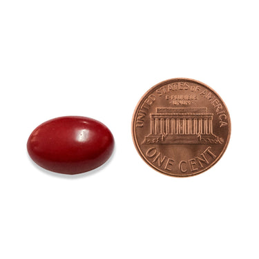 A red softgel capsule being compared to the size of a penny