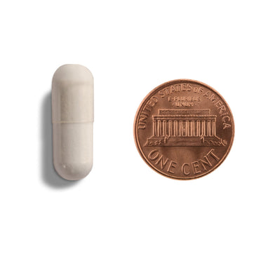 An off-white capsule being compared to the size of a penny