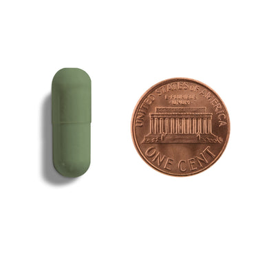 A green capsule being compared to the size of a penny