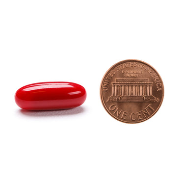 A red softgel capsule being compared to the size of a penny