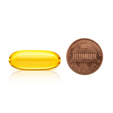 A clear yellow softgel capsule being compared to the size of a penny