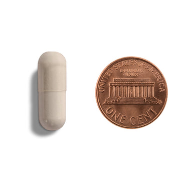 An off-white capsule being compared to the size of a penny