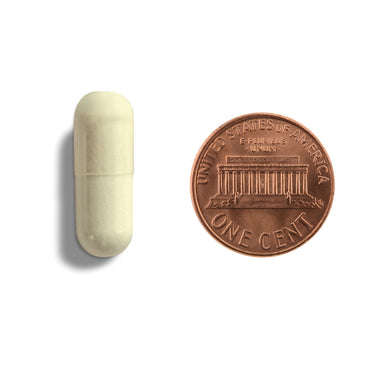 An off-white capsule being compared to the size of a penny