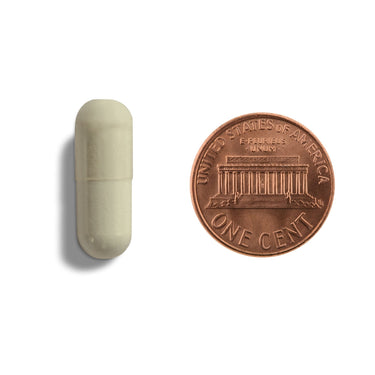 An off-white capsule being compared to the size of a penny
